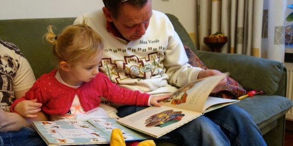 Dad-reads-with-young-daughter-on-sofa-The-effects-of-poverty-on-child-development-NEWS
