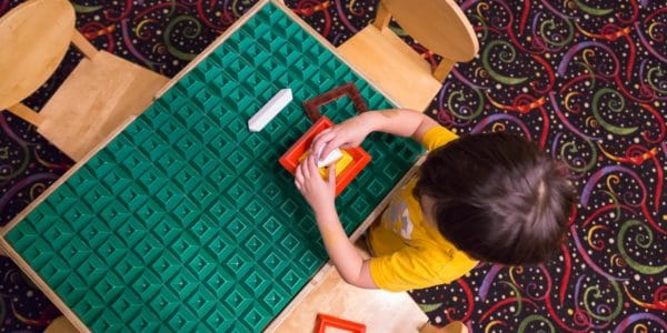 Birds-eye view of a young boy playing with colourful toys at a green table