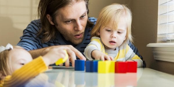 Father playing with two blonde children with coloured bricks