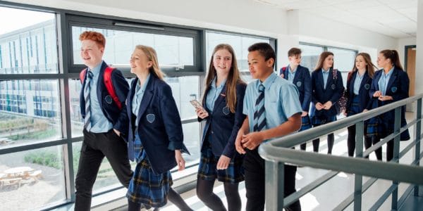 Group of secondary school children in uniform walking through corridor