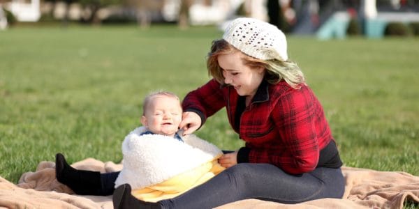Teenage mother with tickling baby's cheek outside on a picnic rug