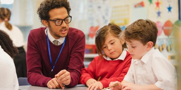 Teacher helps two young boys in school uniform with reading and writing