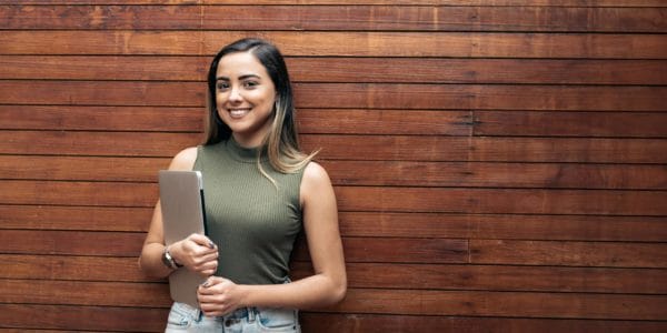 Young woman holding laptop against wooden backdrop