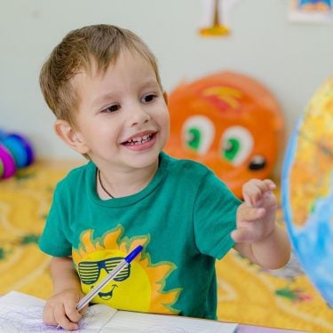 Young boy draws and plays with a globe as part of nursery education