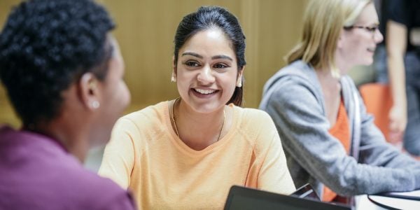 Candid portrait of two young female students with laptop, talking and having fun