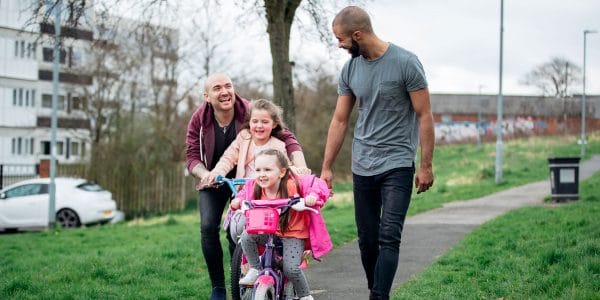 Couple play with their daughters cycling on housing estate