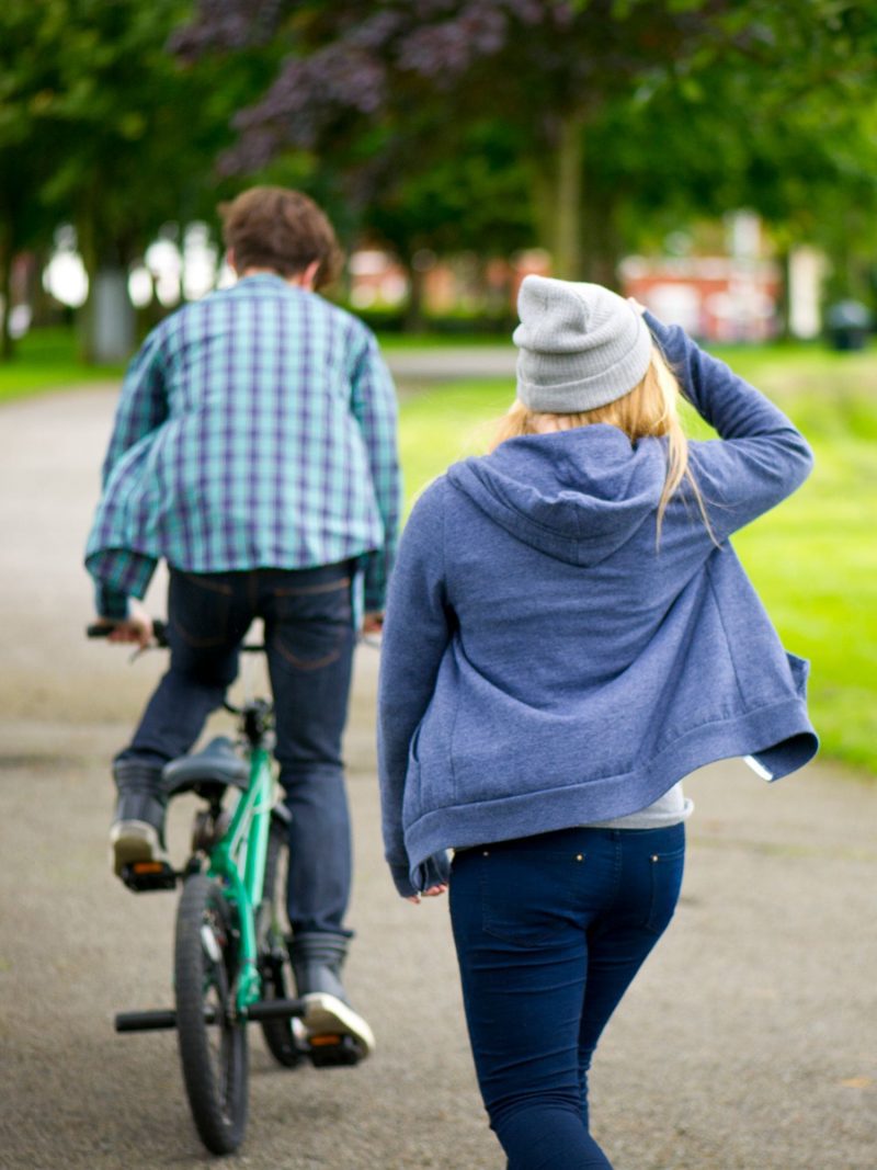 Teenagers wearing hoodies ride a bike in the park