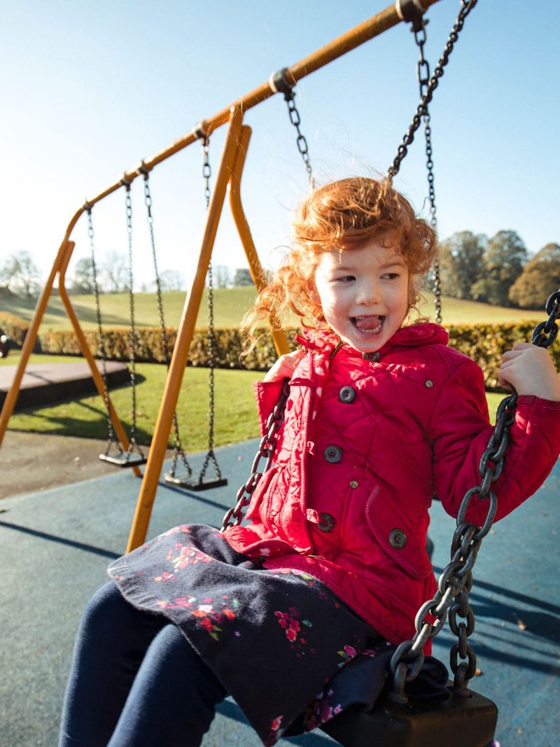 Young girl sticking her tongue out while on a swing at outdoor playground