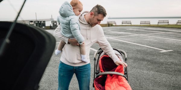 Father holding his child, ready to put them into a push chair, while standing in a car park