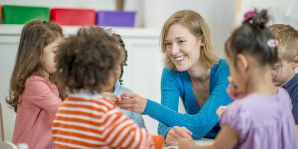 Early years worker sitting at table with children