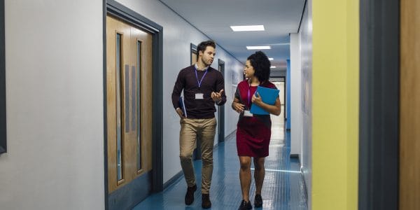 A male and female teacher walk down a school corridor together discussing mental health