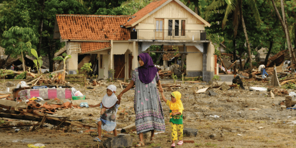 Woman and two children walk through debris outside their destroyed home.