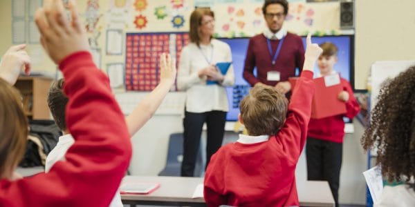 An elementary schoolboy wears a school uniform and presents his work to the class with the support of his teachers beside him. This is a school in Hexham, Northumberland in north eastern England.