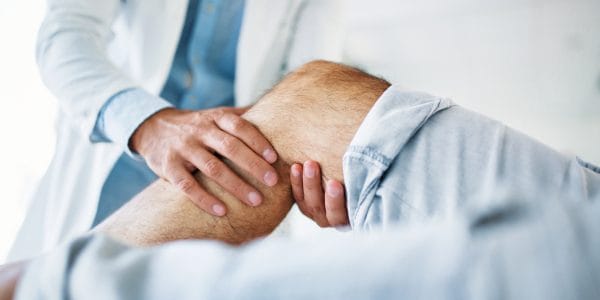 Medical-professional-massages-patient-knee-Understanding-joint-replacement-surgery-decision-making-for-older-patients-PROJ