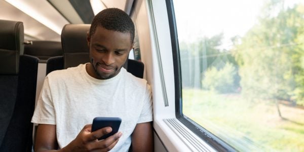 Portrait of a man looking happy traveling by train and checking his social media on a cell phone