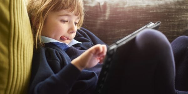 a young girl relaxes with her digital tablet after a hard day at primary school . She is relaxing in an armchair scrolling through the pages .