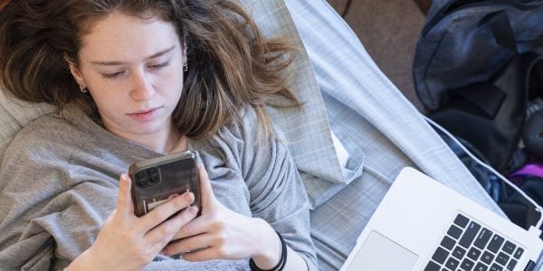 Teenage-girl-looks-at-smartphone-next-to-laptop-Growing-up-under-COVID-19-PROJ