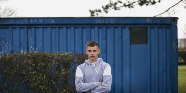 Portrait of a teenager in front of a blue shed, looking at the camera