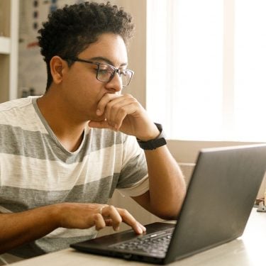 Male secondary school student working at home on laptop