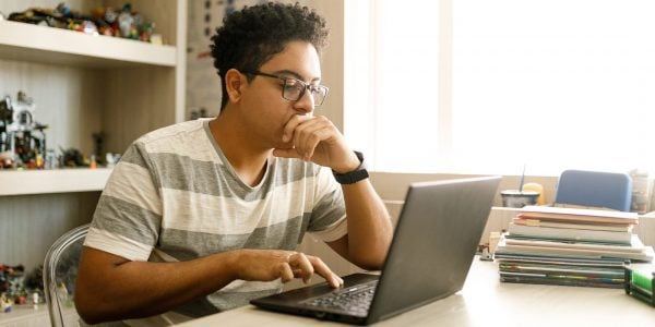 Male secondary school student working at home on laptop