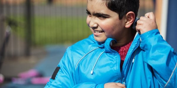 A close-up shot of a young boy standing in the park, holding the zip of his blue jacket.
