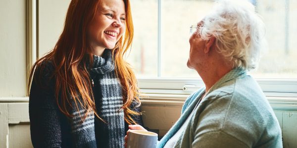 Young woman talking with her mother at home by the window and smiling