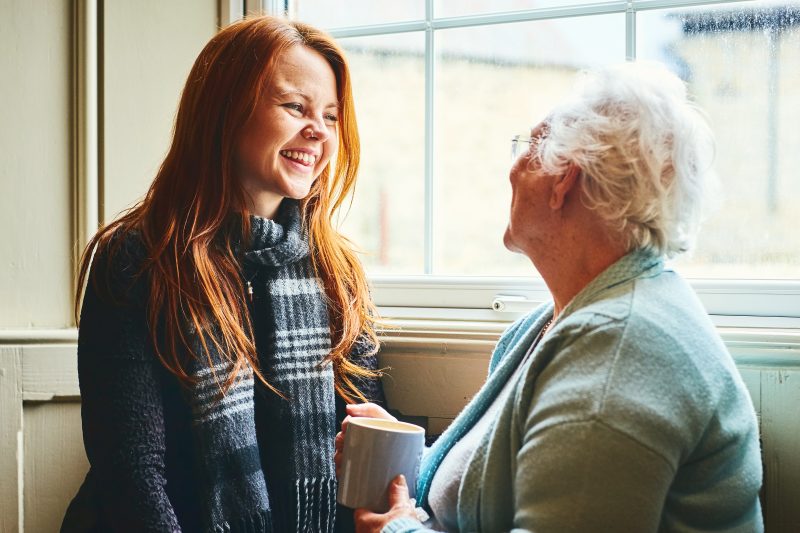 Young woman talking with her mother at home by the window and smiling