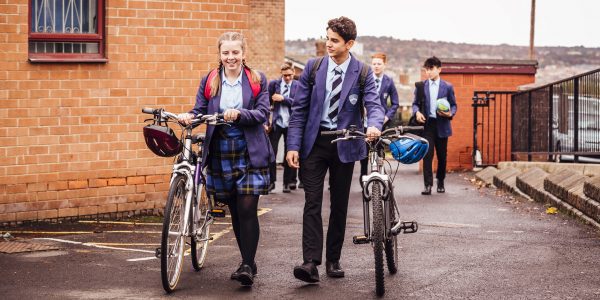 School children with their bicycles in the school yard. Happy as a girl and boy walk pushing them side by side.
