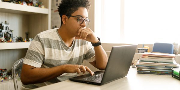 Teenage boy studying with laptop at home