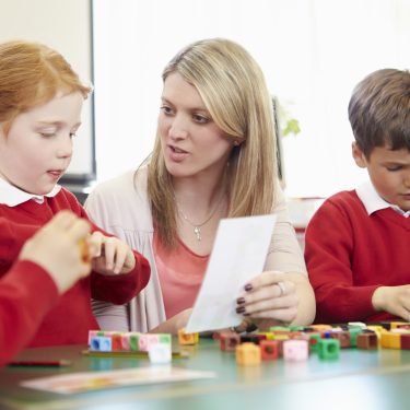 Primary School Pupils And Teacher Working With Coloured Blocks