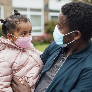 Close up of a young girl and her father wearing protective face masks during the COVID-19 pandemic outside.