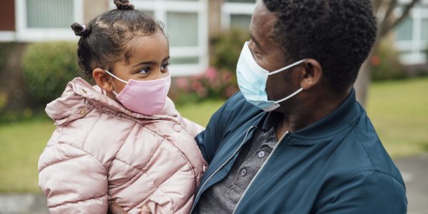 Close up of a young girl and her father wearing protective face masks during the COVID-19 pandemic outside.