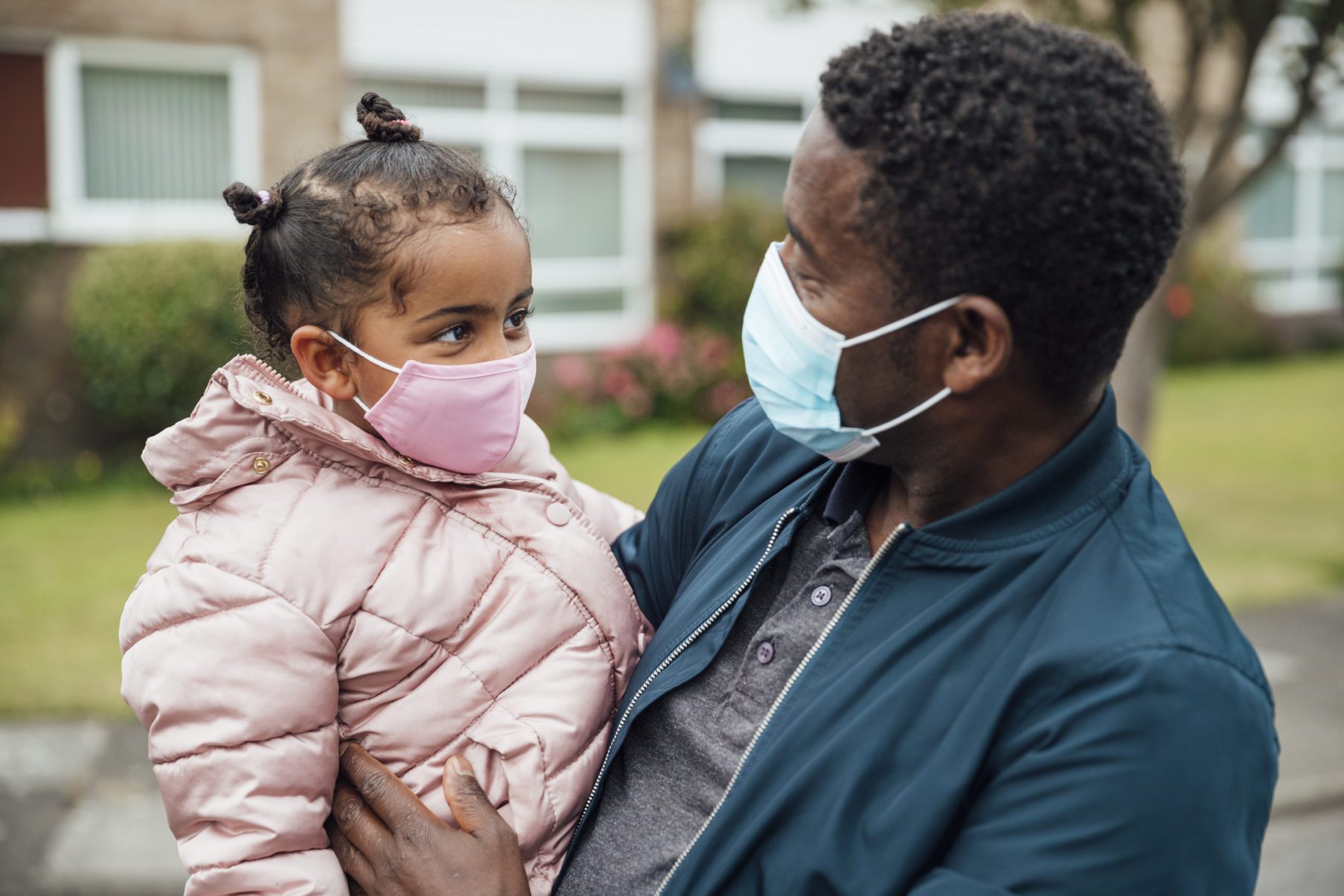 Close up of a young girl and her father wearing protective face masks during the COVID-19 pandemic outside.