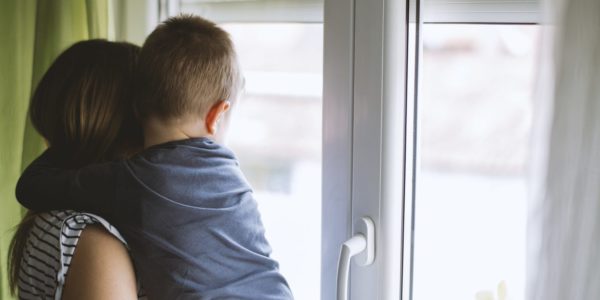 A woman cuddling a boy, looking out of a window