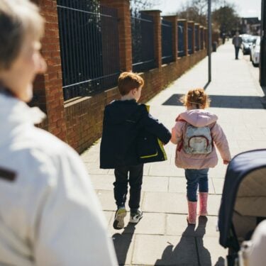 Two children walk ahead of two adults, one pushing a pram