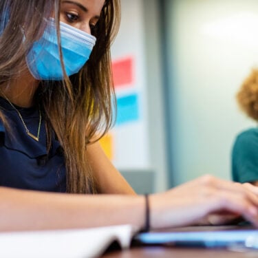 Side view of two female high school students in classroom working on laptops social distancing. Student in foreground is in focus and student in background is blurred