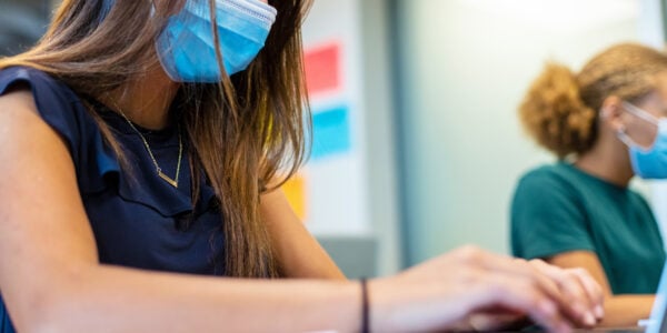 Side view of two female high school students in classroom working on laptops social distancing. Student in foreground is in focus and student in background is blurred