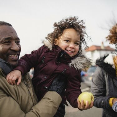 Grandparents having fun outdoors with their granddaughter, who is eating an apple and laughing: Understanding family and community vulnerabilities in transition to net zero