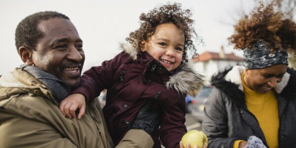 Grandparents having fun outdoors with their granddaughter, who is eating an apple and laughing: Understanding family and community vulnerabilities in transition to net zero