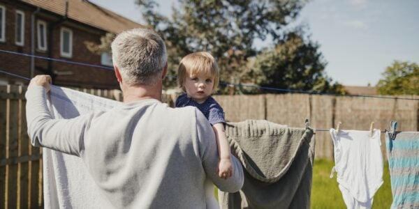 COVID Realities: an older father holds a small child while hanging washing on the line outside