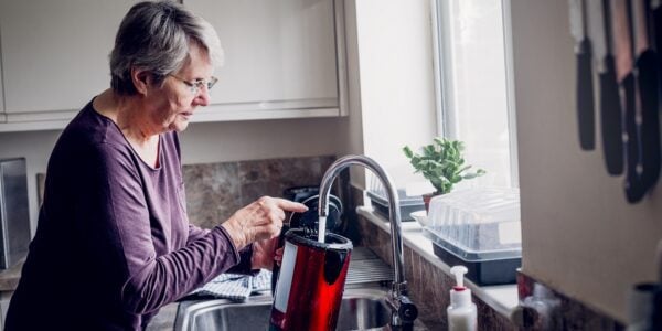An older woman fills up the kettle in her kitchen