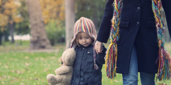 A child holding a teddy bear holding the hand of an adult while walking in a park