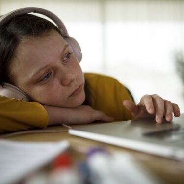 A child with headphones sitting on her own using a laptop