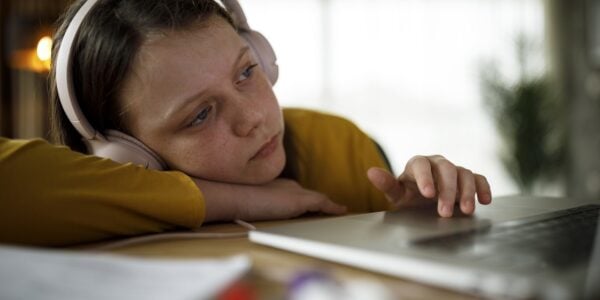 A child with headphones sitting on her own using a laptop