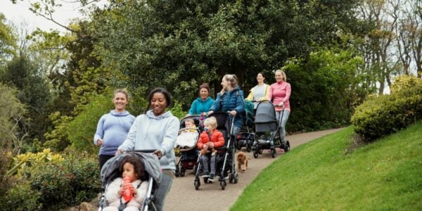 A group of women walk in a park with their children in pushchairs