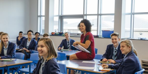 Pioneering study reveals teaching techniques which boost exam performance: a teacher sits on a desk among her secondary school pupils, all looking at the board