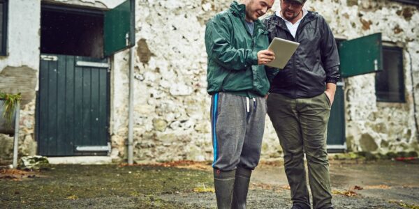 Two cheerful farmers standing outside a farm building looking at a tablet