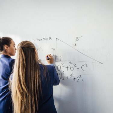 Two secondary school pupils solve a maths problem together on a whiteboard