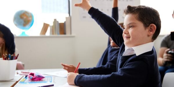 A primary school boy and his classmates raise their hands in a lesson