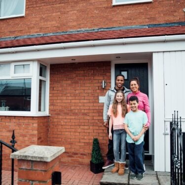 Mother, father, son and daughter standing in front of their house